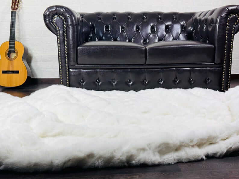 White Rabbit Fur Throw Blanket - Tatifurs on a dark wooden floor near a leather couch and guitar.