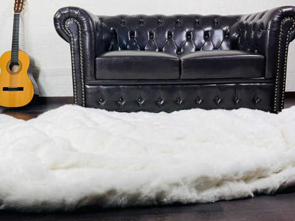 White Rabbit Fur Throw Blanket - Tatifurs on a dark wooden floor near a leather couch and guitar.