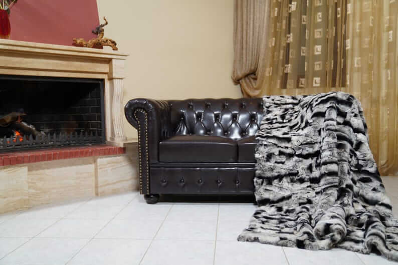 Rabbit Blanket Throw Chinchilla Rex - Tatifurs draped on a cozy leather couch by the fireplace in an elegant living room.