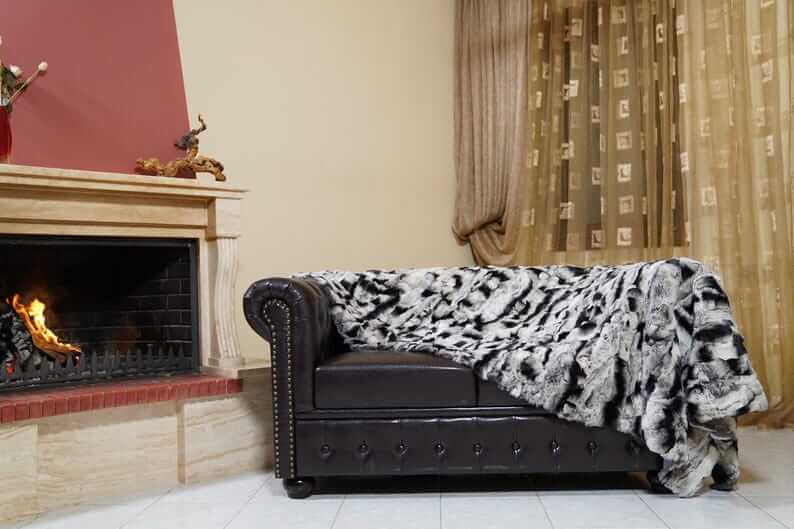 Rabbit Blanket Throw Chinchilla Rex - Tatifurs draped over a stylish couch near a fireplace in an elegant living room.