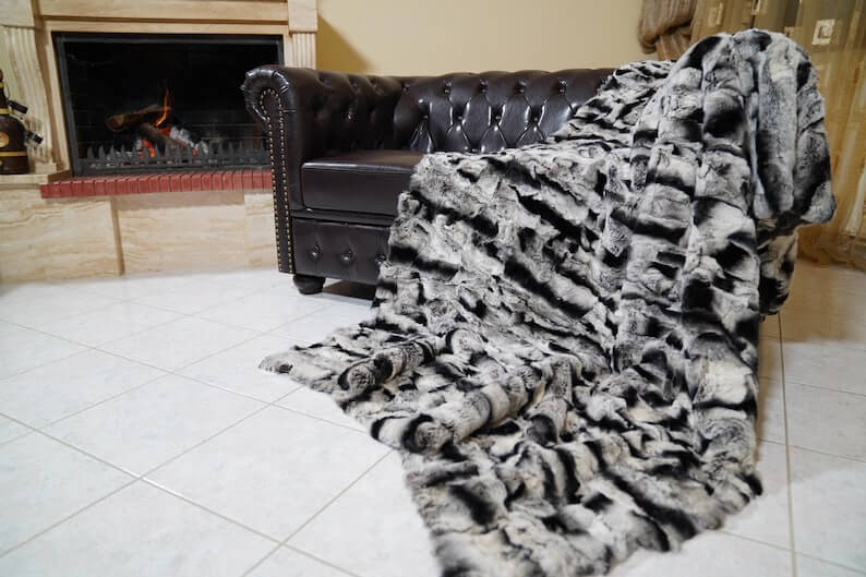 Rabbit Blanket Throw Chinchilla Rex - Tatifurs draped over a couch near a fireplace, showcasing its luxurious fur texture.