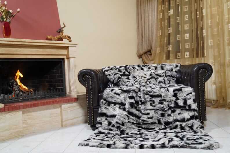 Rabbit Blanket Throw Chinchilla Rex - Tatifurs draped over a leather couch by the fireplace, showcasing luxury and softness.