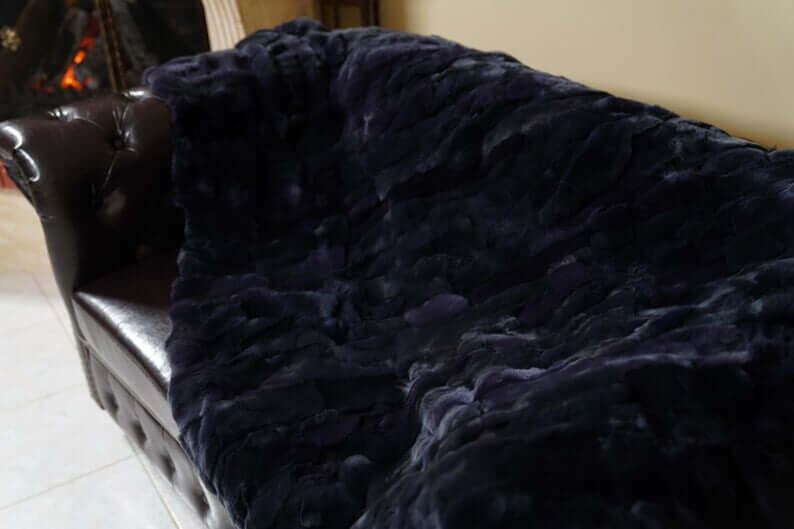 Double Sided Fur Rex Rabbit Blanket Throw Dark Blue draped over a leather sofa, showcasing its rich texture.