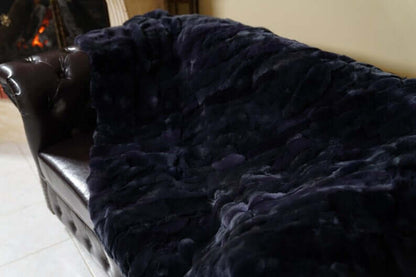 Double Sided Fur Rex Rabbit Blanket Throw Dark Blue draped over a leather sofa, showcasing its rich texture.