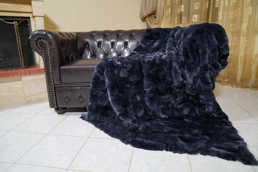 Double Sided Fur Rex Rabbit Blanket Throw Dark Blue draped on a stylish leather sofa in a cozy living room.