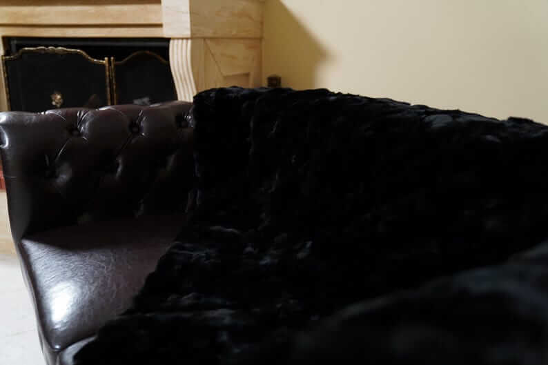 Rabbit Blanket Throw Rex Black - Tatifurs draped over a luxurious leather couch, showcasing its softness and elegance.