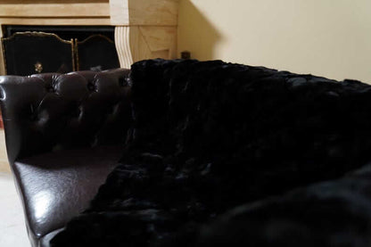 Rabbit Blanket Throw Rex Black - Tatifurs draped over a luxurious leather couch, showcasing its softness and elegance.