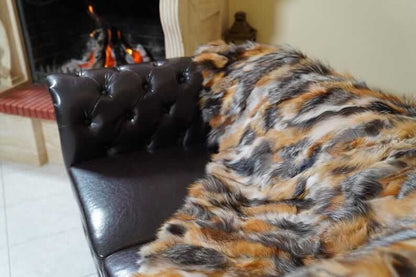 Fur Throw Blanket Natural Gross Fox – Luxury - Tatifurs draped over a stylish leather chair by a fire.