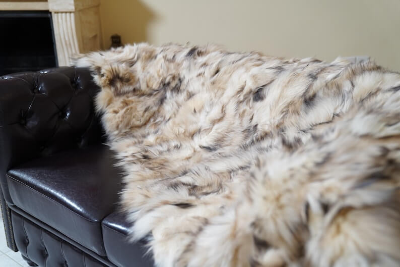 Fox Fur Blanket Throw Double Sided Iceberg Beige draped on a dark leather couch, showcasing its luxurious texture and warmth.
