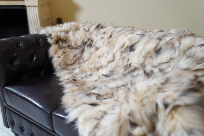 Fox Fur Blanket Throw Double Sided Iceberg Beige draped on a dark leather couch, showcasing its luxurious texture and warmth.