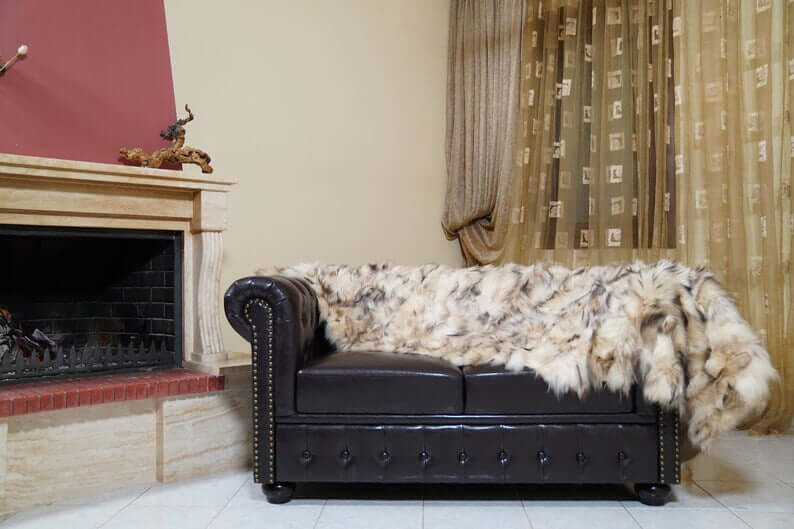 Fox Fur Blanket Throw Double Sided Iceberg Beige draped over a luxurious dark leather couch in a cozy living room setting.