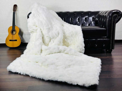 White Rabbit Fur Throw Blanket - Tatifurs displayed on a stylish black sofa with a guitar.