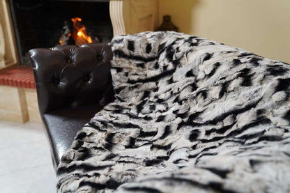 Rabbit Blanket Throw Chinchilla Rex - Tatifurs draped on a couch near a cozy fireplace, showcasing luxury and softness.