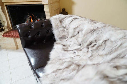 Fox Fur Blanket Throw Blue Natural - Tatifurs draped over a stylish leather chair next to a cozy fireplace.