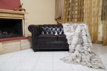 Fox Fur Blanket Throw Blue Natural - Tatifurs draped over a stylish black leather sofa in a cozy living room setting.