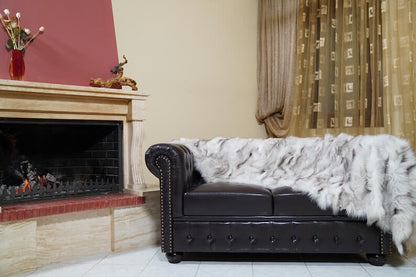 Fox Fur Blanket Throw Blue Natural - Tatifurs styled on a leather couch beside a fireplace.