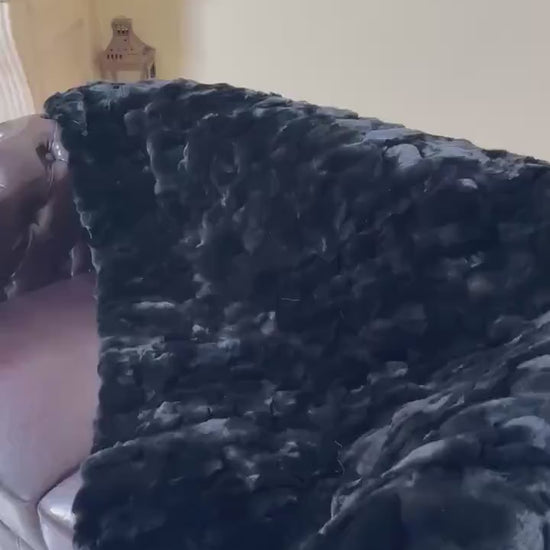 Double Sided Fur Rex Rabbit Blanket Throw Black draped over a couch, showcasing its luxurious texture.