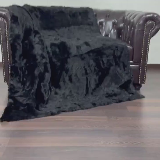 Rabbit Fur Blanket Throw Black - Tatifurs displayed on a brown leather sofa with a guitar in the background.