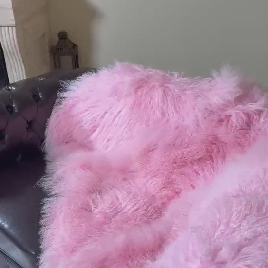 Wool Sheepskin Mongolian Blanket Throw Pink - Tatifurs draped over a stylish couch, showcasing its fluffy texture.