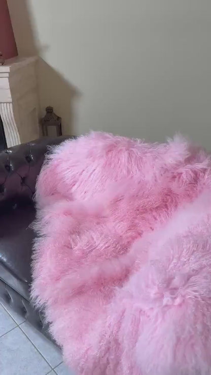 Wool Sheepskin Mongolian Blanket Throw Pink - Tatifurs draped over a stylish couch, showcasing its fluffy texture.