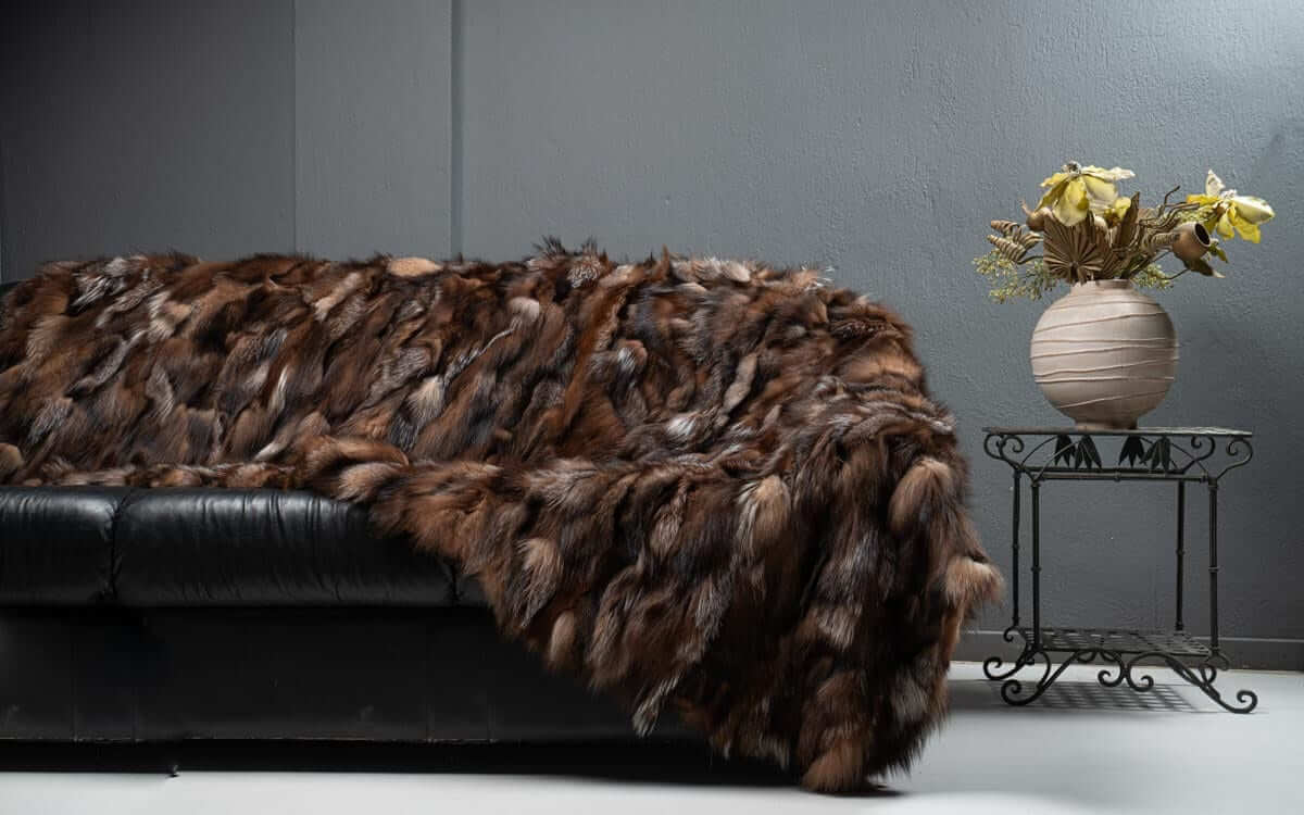 Fox Fur Blanket Throw Crystal Dark - Tatifurs draped on a black couch, showcasing its rich brown tones and texture.