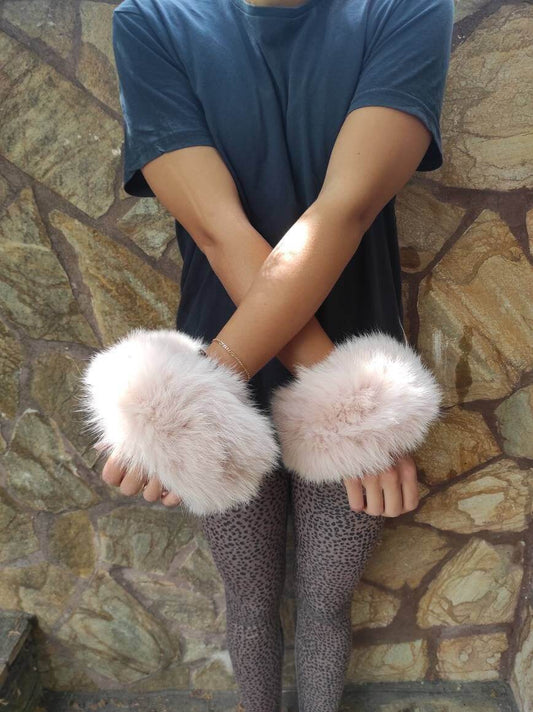Woman wearing baby pink fox fur cuffs on wrists showing soft feminine blush color
