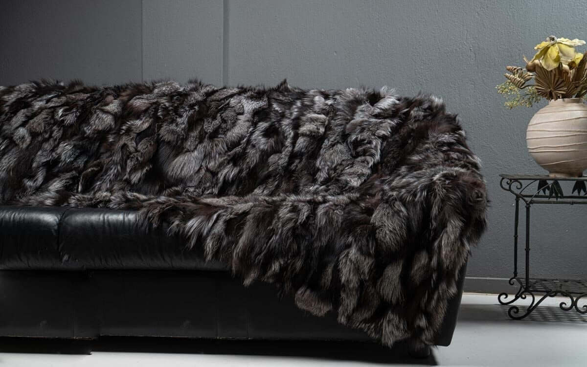 Fox Fur Blanket Throw Silver Dark - Tatifurs draped elegantly on a black sofa, showcasing rich charcoal and silver tones.